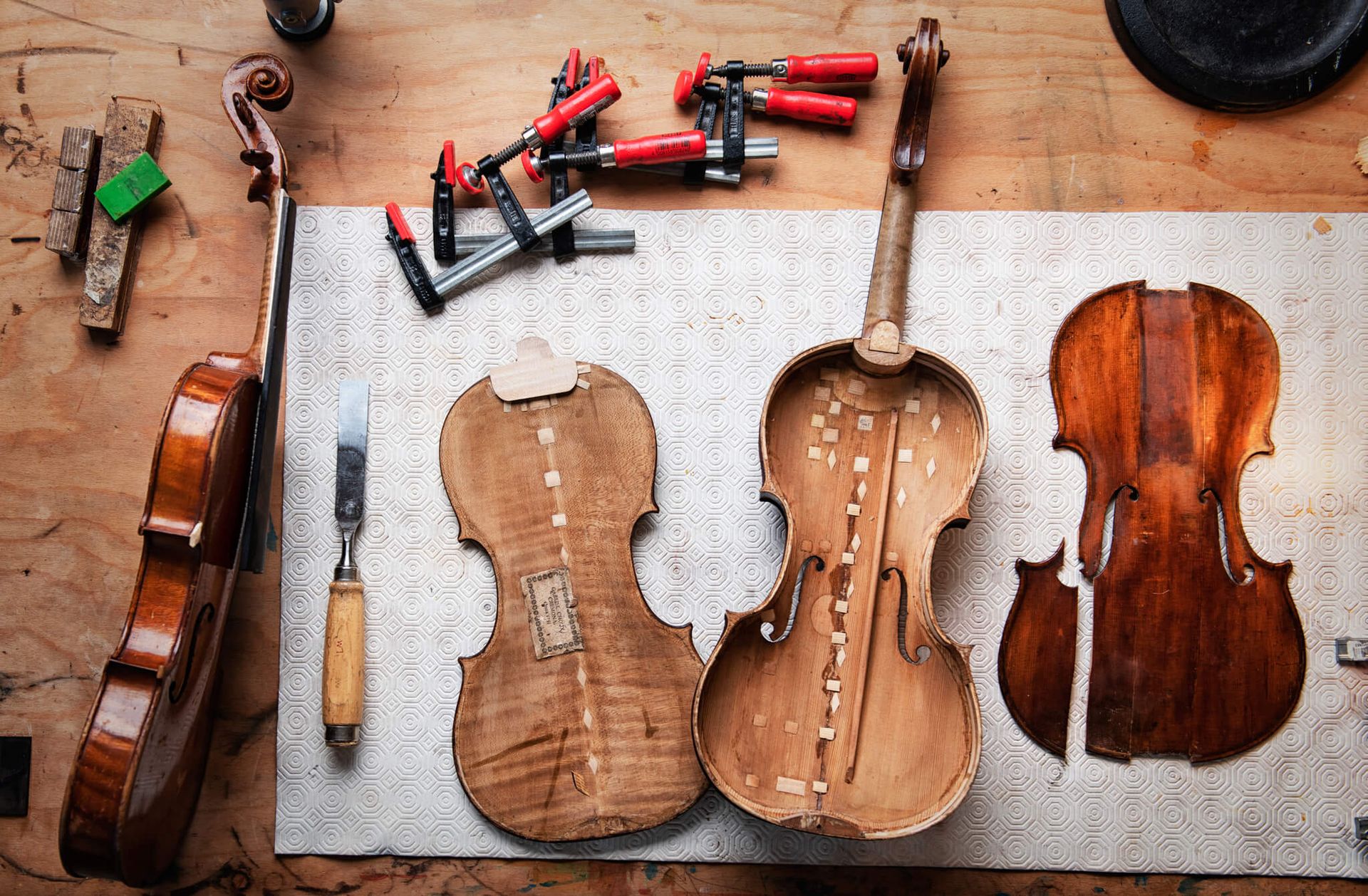 Einzelne Bauteile einer Geige liegen auf einer Unterlage auf einem Tisch. Drumherum liegen Werkzeuge.