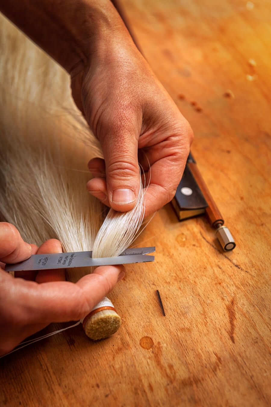 Zwei Hände in Nahaufnahme. Sie messen einen Strang Rosshaar für einen Geigenbogen ab.