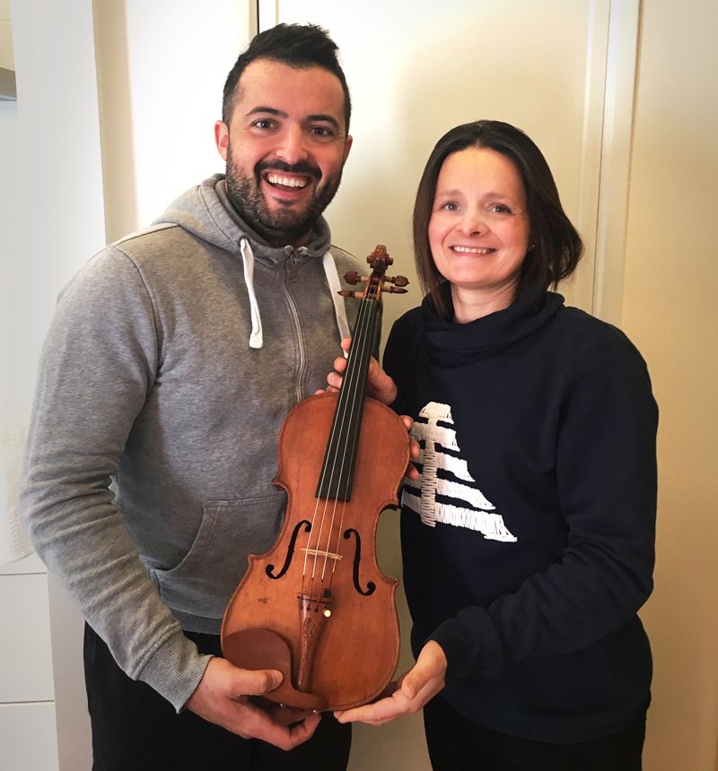 Judith Bauer steht links neben Jordi Rodriguez Cayuelas. Beide halten zusammen eine Geige fest.
